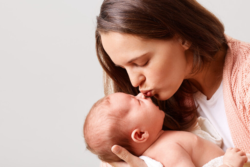 A mother tenderly kisses her newborn, showcasing loving maternal care.