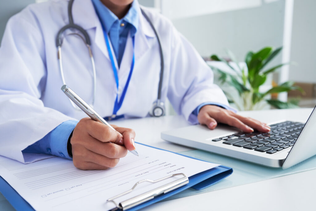 Female doctor writing on a medical form while typing on a laptop at Eva WomanCare Clinic Vashi