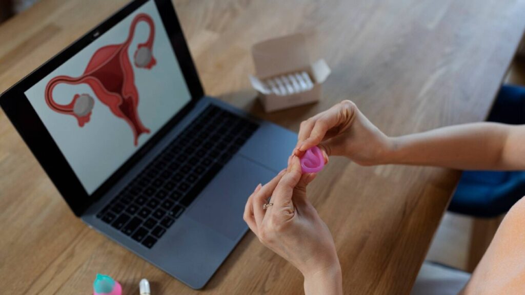 Person learning menstrual cup usage with laptop educational guide.