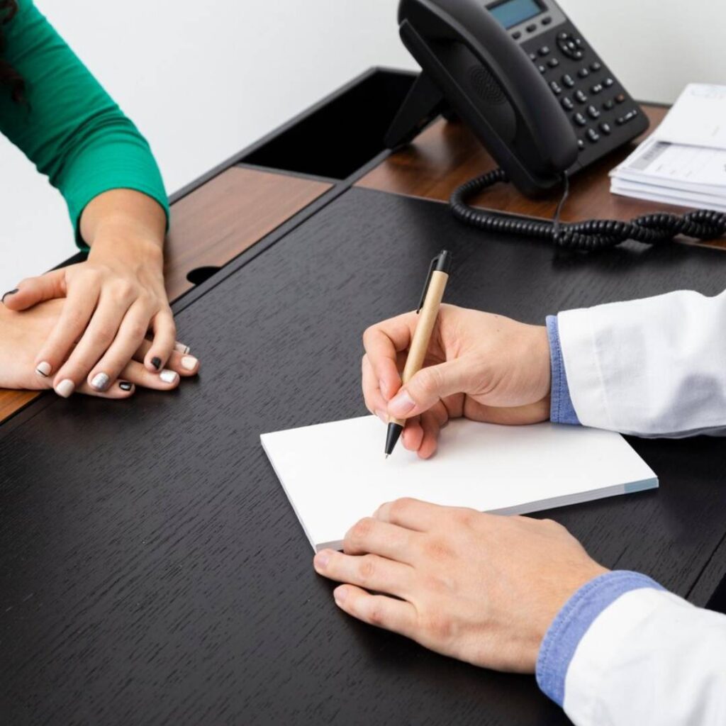 Doctor writing notes during a consultation at a healthcare clinic desk.