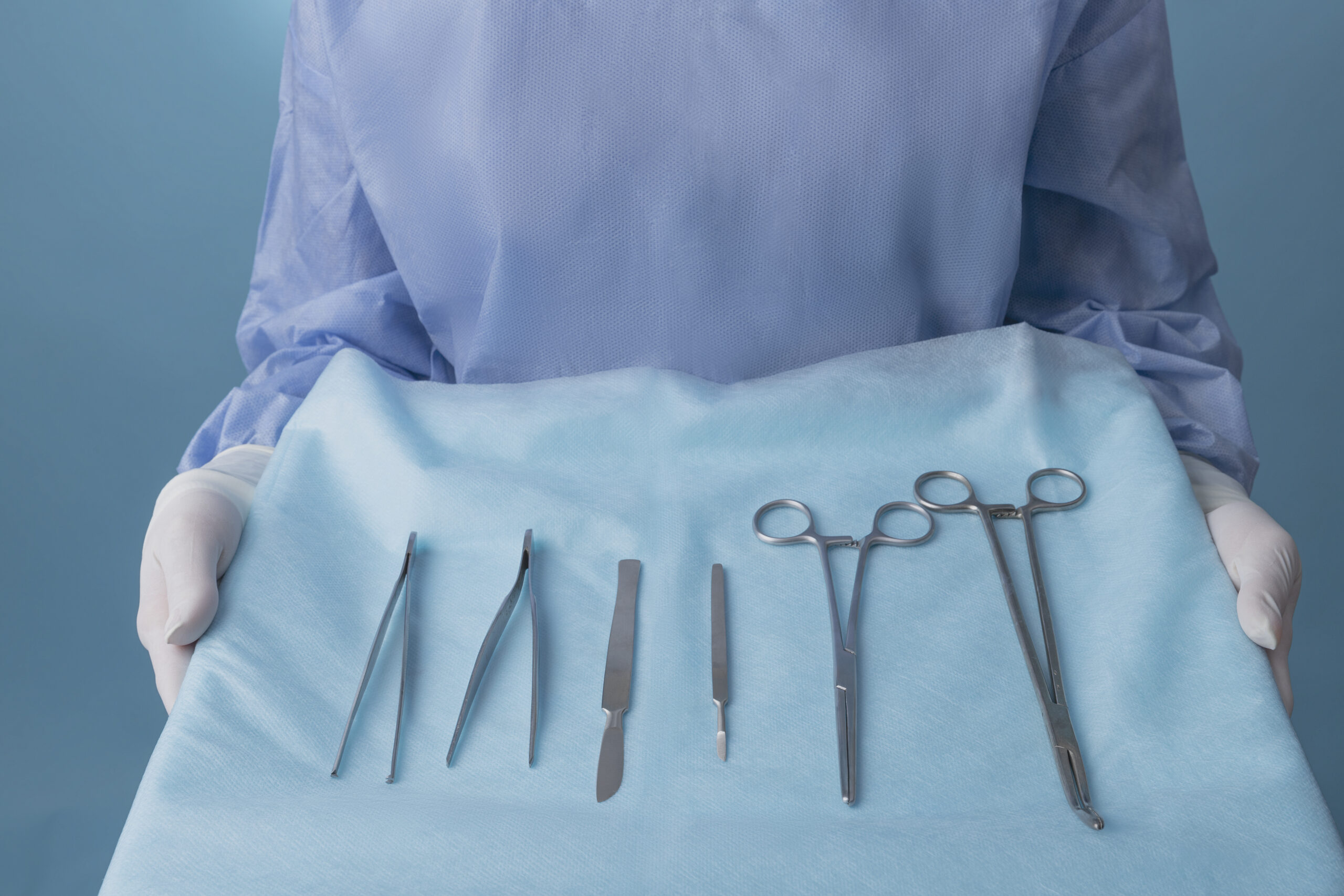 Medical professional holding surgical tools wrapped in a blue cloth