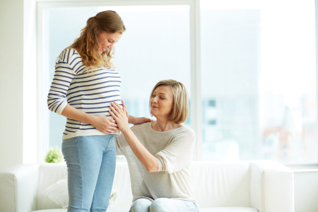 Pregnant woman being lovingly supported by a friend in a bright living room.