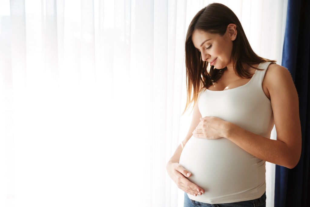 Smiling pregnant woman gently touching her belly — high-risk pregnancy care at Eva WomanCare Clinic Vashi