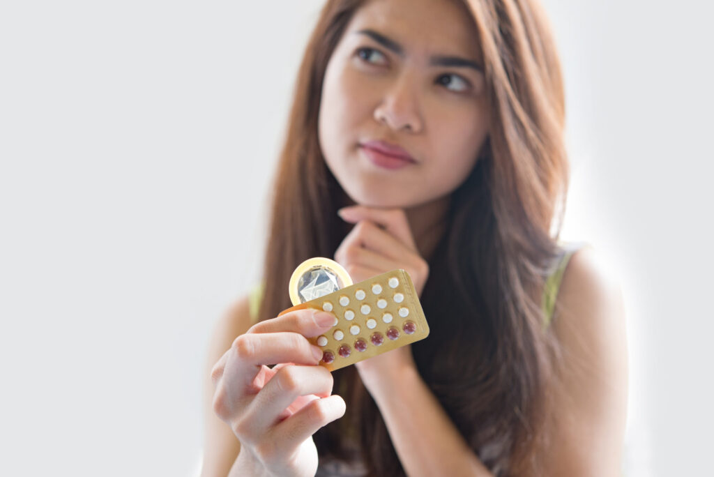 Woman holding birth control and condom thoughtfully.